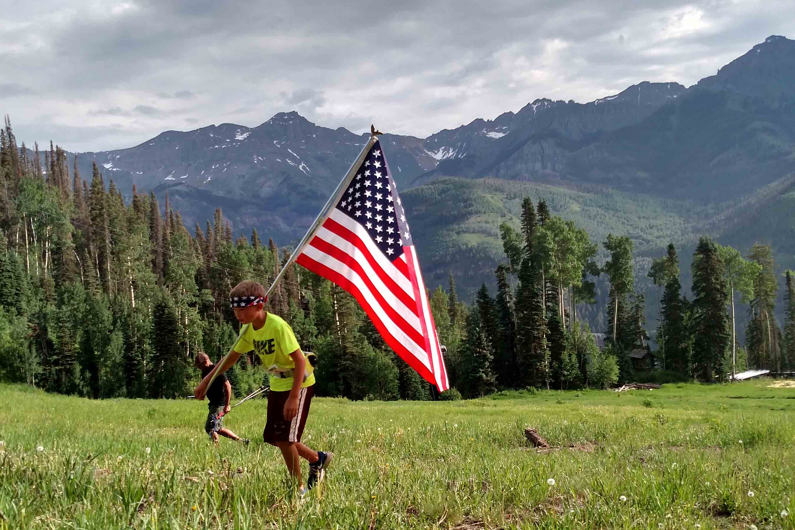 Photo of child carrying flag up a green hillside