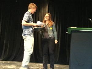 A young man recieving a reward from a smiling women on a stage